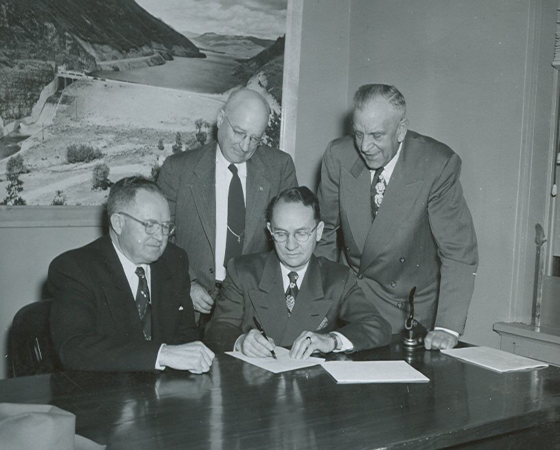 Photo of men signing papers around a table.